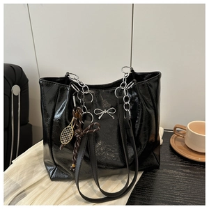 Detail of black glossy tote bag with silver bow accent and metal chain shoulder strap