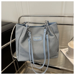 Detail of blue woven texture tote bag featuring silver chain strap and leather handle