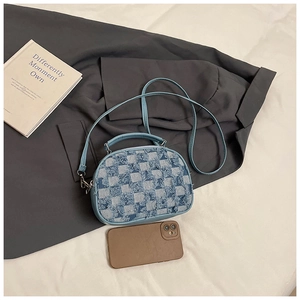 Detailed top view of light blue checkerboard denim handbag with fringe and leather strap