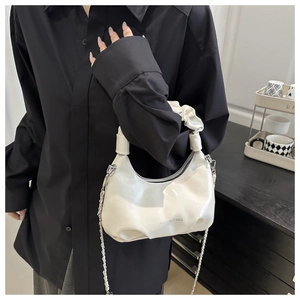 Close-up of white glossy patent leather handbag with pleated handle and silver chain strap