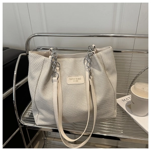 Close-up of beige woven tote bag showing V-pattern texture and silver chain strap details