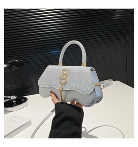 Detail of silver sequined handbag with gold SS logo and tassel on white table