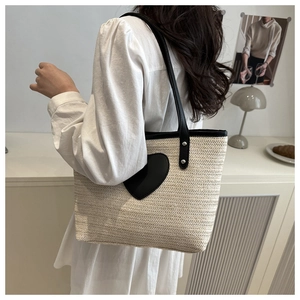 Détail du sac cabas en paille avec écusson cœur noir et bandoulière sur le mannequin
