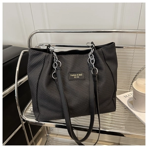 Close-up of black tote bag with twill texture and silver chain leather strap on shelf