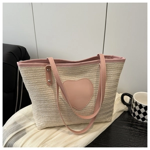 Vue détaillée du sac cabas en paille avec écusson cœur en cuir rose et poignées robustes