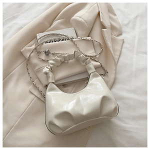 Detail of minimalist beige pleated handbag with metal ball chain and ruffled handle