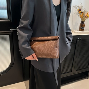 Brown woven leather envelope clutch bag held by model in a modern indoor setting