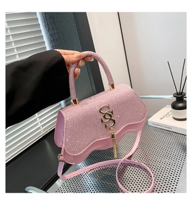 Pink sequin handbag with wave base, gold S-logo, and elegant tassel detail held by hand