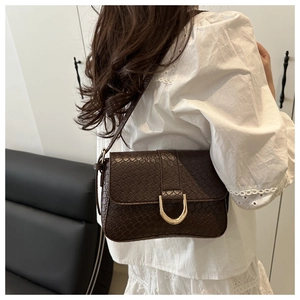 Detail of dark brown faux crocodile leather shoulder bag with golden D-ring buckle closure