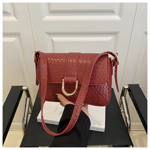 Detail of burgundy baguette bag with woven texture, golden D-buckle and wide strap