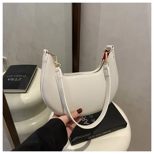 Detail of white half-moon bag featuring red lining, lychee texture, and gold hardware