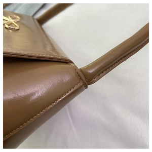 Détail de la boucle dorée et des coutures sur un sac en cuir marron brillant