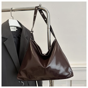 Detail of dark brown glossy leather tote bag showing adjustable strap and metallic buckles