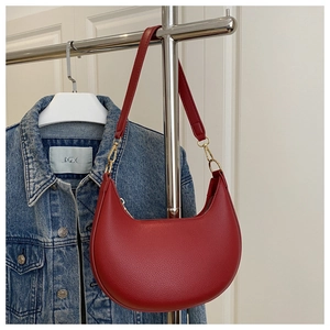 Detail of red crescent shoulder bag with pebbled leather texture and gold metal hooks