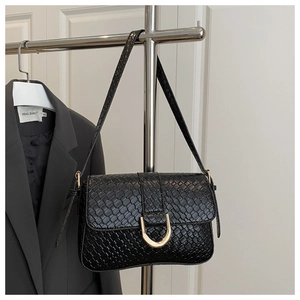 Close-up of black woven shoulder bag featuring a prominent gold horseshoe-shaped buckle
