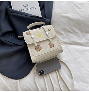 Detail of cream white backpack with cartoon embroidery and metal buckles on bed