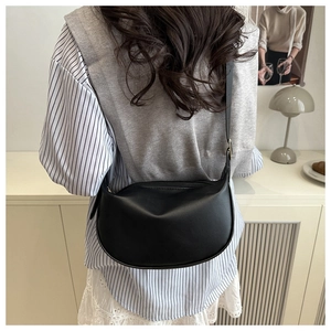 Close-up of matte black crescent bag worn over the shoulder against a vintage home setting