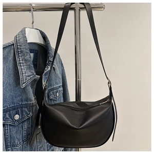 Detail of a black leather crescent shoulder bag with adjustable strap and metal zipper