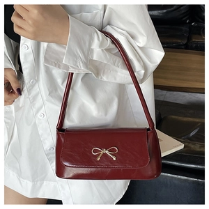 Détail du sac baguette rouge foncé avec boucle nœud doré sur similicuir lisse