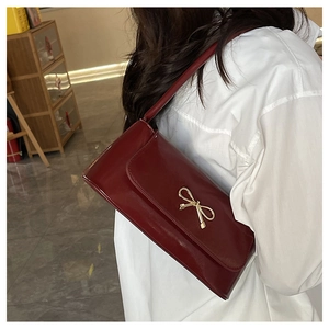 Modèle portant un sac sous le bras bordeaux avec nœud doré et finition brillante