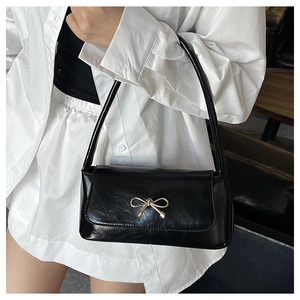Détail d'un sac baguette noir brillant avec un nœud doré sur une chemise blanche