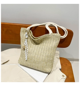 Detail of hand-woven straw tote with thick white rope handles and decorative pendant