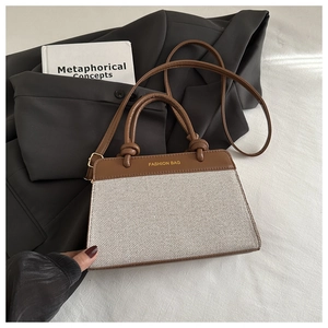 Detail of a brown leather and canvas bag next to a grey blazer and book