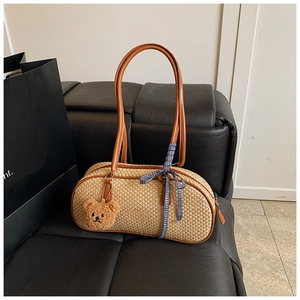 Detail view of woven straw handbag with brown leather handles and plush bear charm