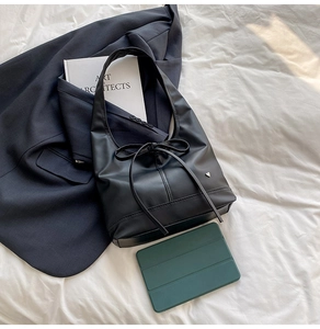 Détail d'un sac cabas noir avec nœud en cuir et pendentif cœur argenté sur lit blanc