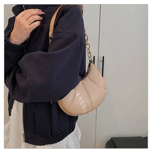 Detail of beige crescent underarm bag with pleated leather texture and gold chain strap