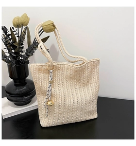 Close-up of beige woven tote bag with striped rope knot and golden bell charm