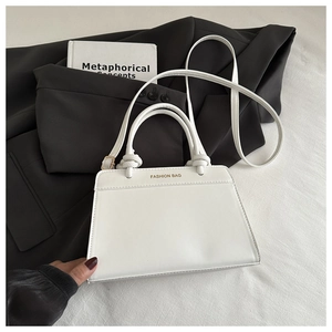 Close-up of white leather tote bag with knotted handles and gold fashion bag logo
