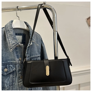 Detail view of a black minimalist rectangular shoulder bag with a gold metal buckle on a rack
