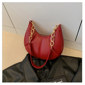 Detail of red crescent bag with vertical pleated texture and bold gold chain strap