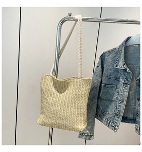 Detail view of woven straw tote bag with white cotton rope handles on a hanger