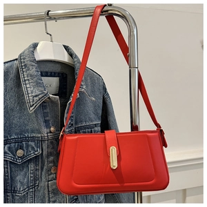 Detail of red baguette bag with golden buckle hanging on clothes rack with denim jacket