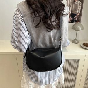 Minimalist black leather half-moon crossbody bag shown in a stylish home setting