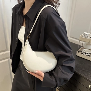 Minimalist white crescent shoulder bag in textured leather worn by a model in casual style