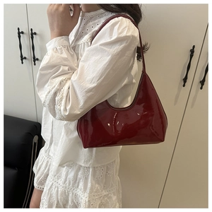 Close-up of a red patent leather crescent bag with embossed logo and metal zipper detail