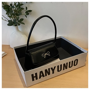 Détail du sac sous le bras noir brillant avec nœud en métal doré sur présentoir