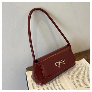 Détail d'un sac à bandoulière en cuir verni bordeaux avec boucle nœud doré sur un livre