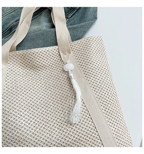 Détail du sac cabas beige tressé avec bandoulière large et pompon décoratif blanc