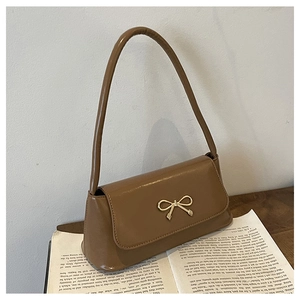 Détail macro du cuir verni caramel et de la boucle nœud dorée sur un sac à main femme