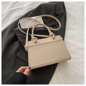 Detail of beige square crossbody bag with gold rings on grey suit background