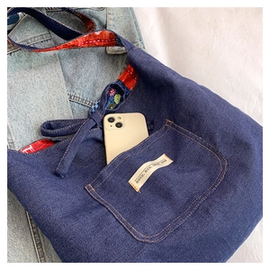 Detail of denim tote bag with patterned strap and a phone in the front pocket