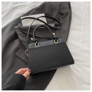 Close-up of minimalist black leather tote bag with elegant gold rings and embossed lettering