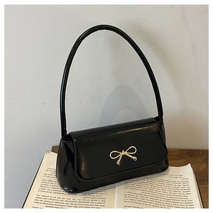 Détail d'un sac baguette en cuir verni noir avec boucle nœud doré sur un livre ancien