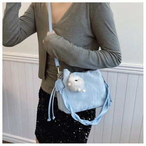 Détail de sac seau bleu clair texturé avec un charmant porte-clés lapin en peluche blanc