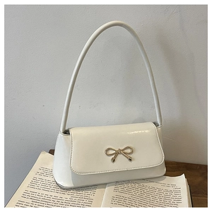 Détail d'un sac sous le bras en cuir blanc avec nœud doré posé sur un livre ouvert