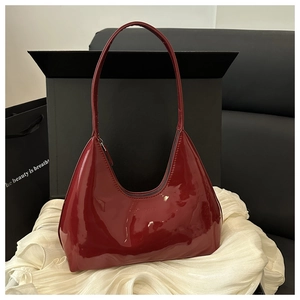 Detailed macro view of glossy burgundy patent leather hobo bag texture and zipper strap